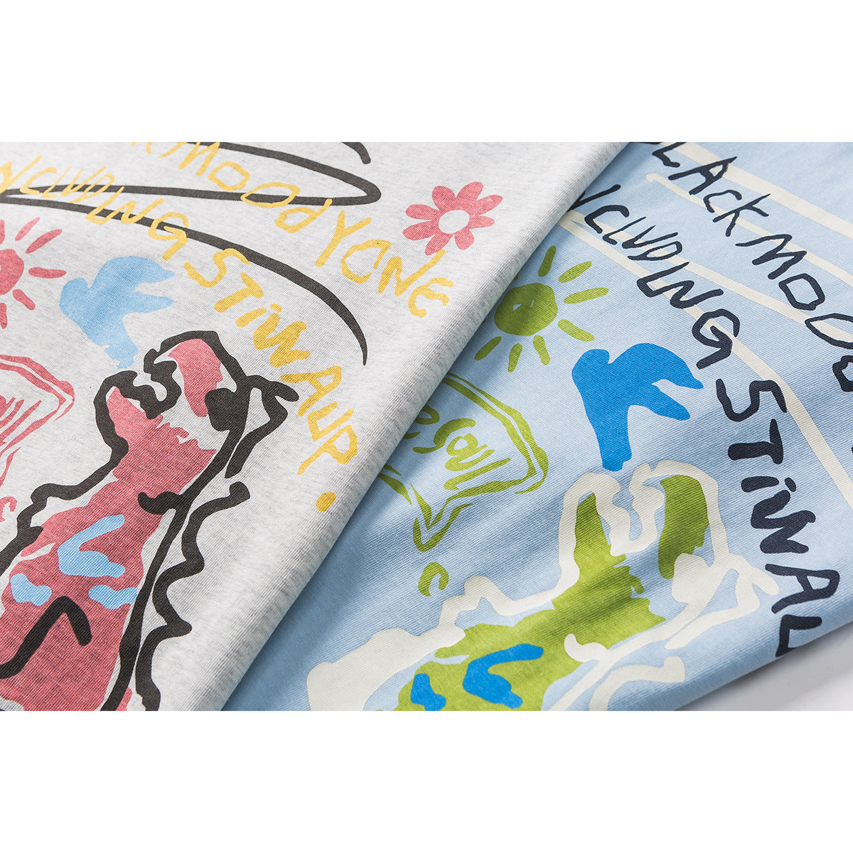 Close-up of gray and light blue T-shirts with colorful printed lettering and playful illustrations.