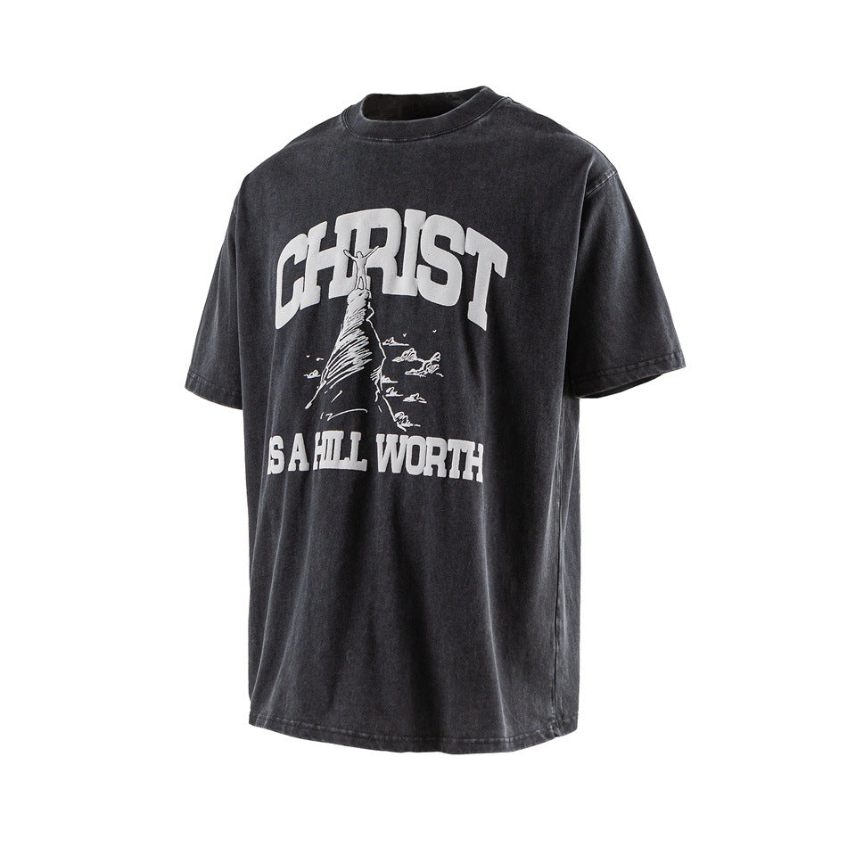 Black washed short-sleeve T-shirt with white 'CHRIST IS A HILL WORTH' hill graphic, angled front view