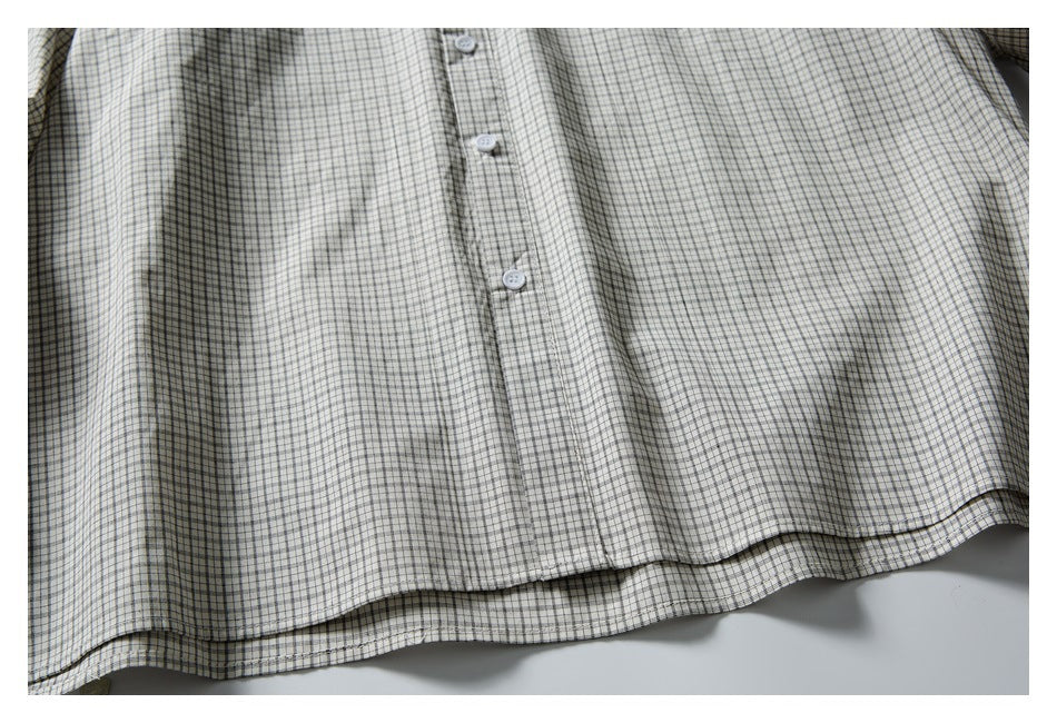 Close-up of the button placket and lower front of an off-white shirt with a fine black and gray check pattern.