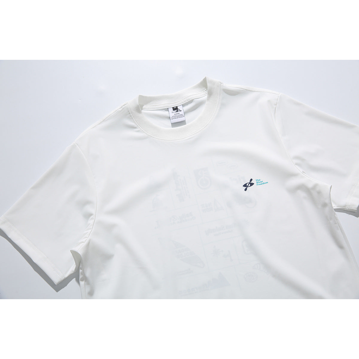 Close-up of a white crew-neck T-shirt with a small paddle emblem and turquoise text on the chest; faint graphics show