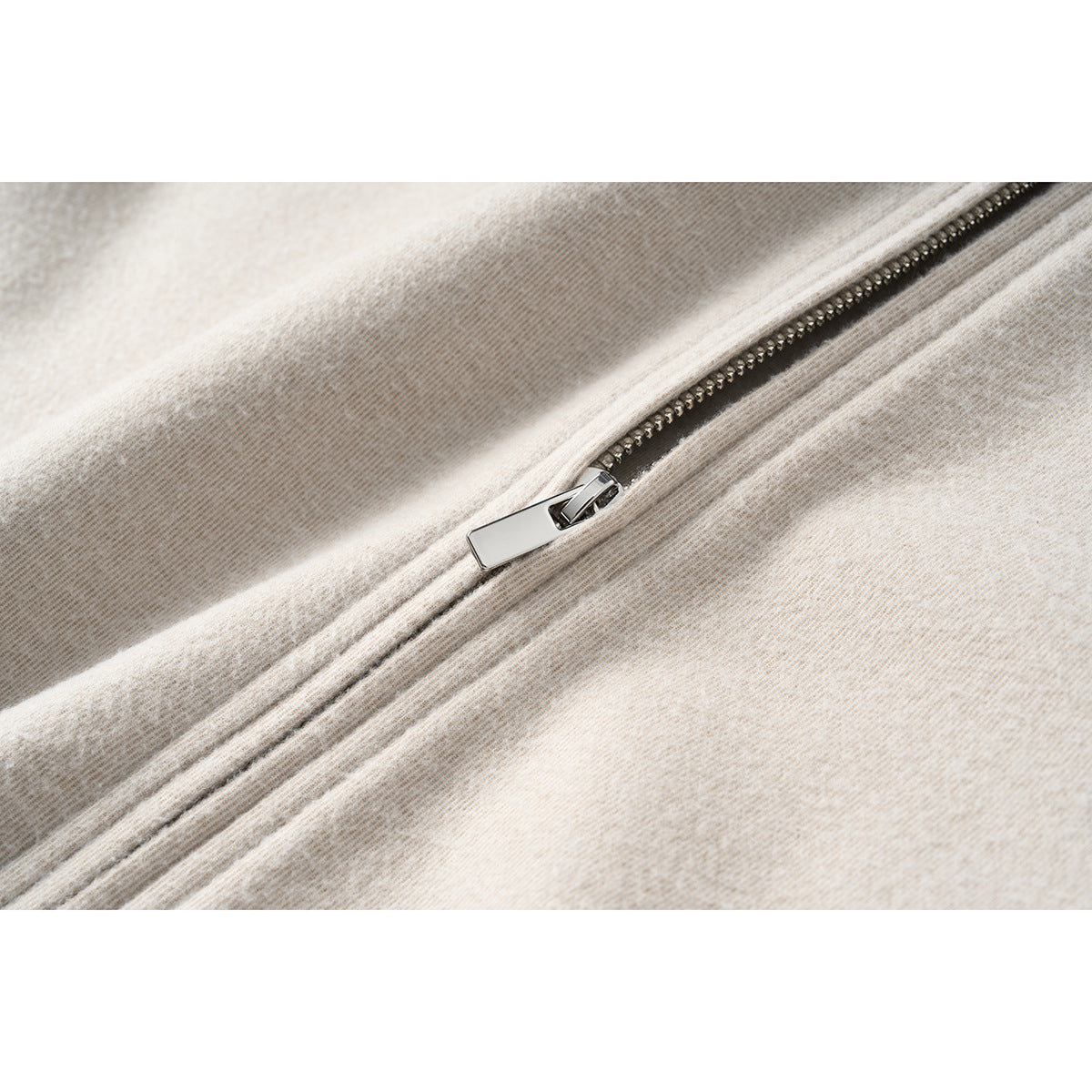 Close-up of the jacket's diagonal silver zipper and textured light beige fabric.