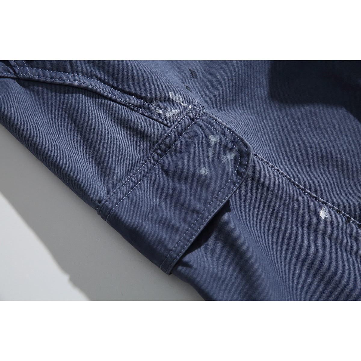 Close-up of a blue-gray cargo pocket flap and seams, with scattered light distressed marks.