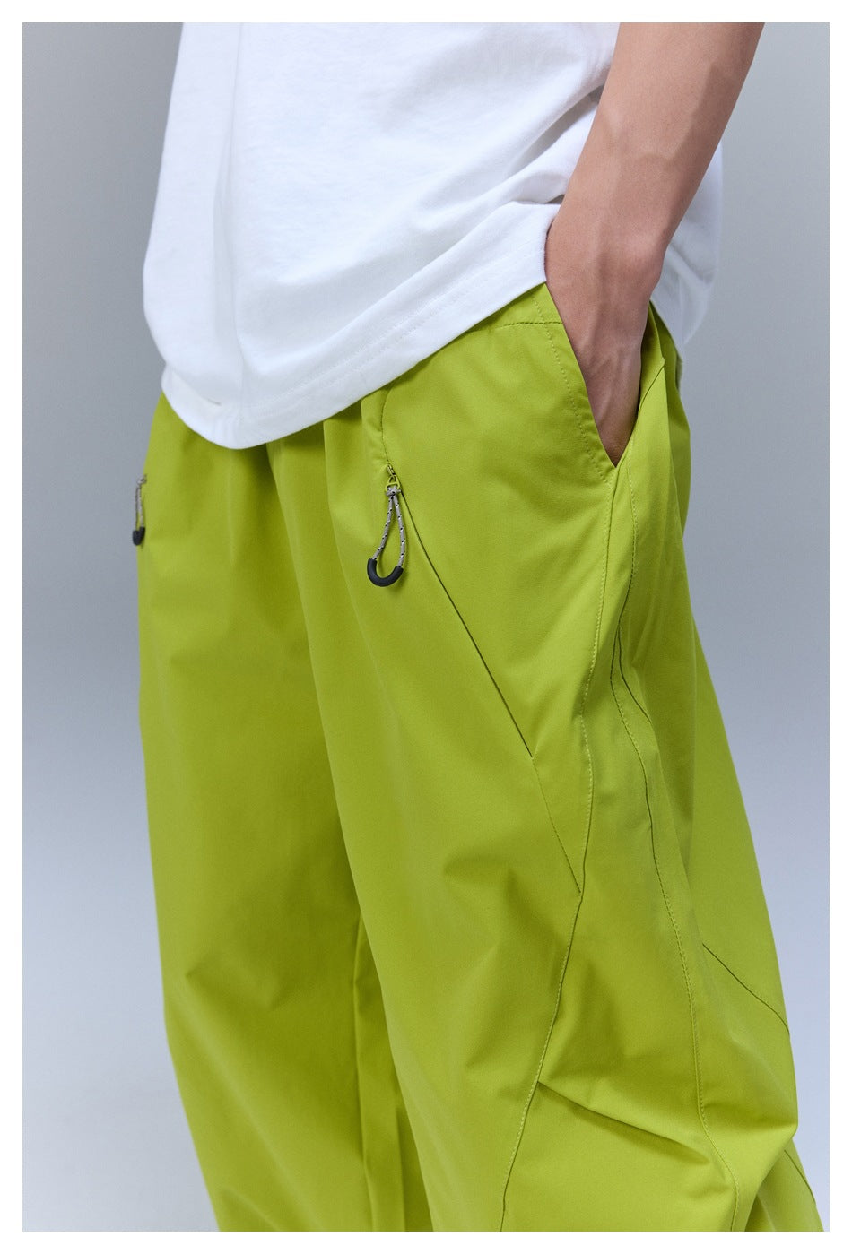 Close view of lime-green pants worn with a white shirt, showing a hand in the pocket and a zip pocket with a hook pull.