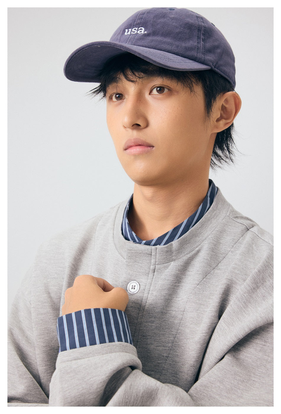Close-up of a model wearing the gray jacket over a blue striped shirt, with a purple cap.