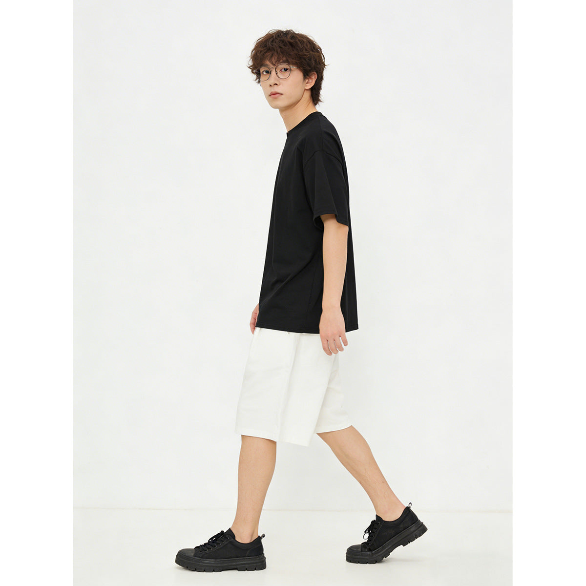 Side view of a model wearing a plain black short-sleeve T-shirt and white shorts.