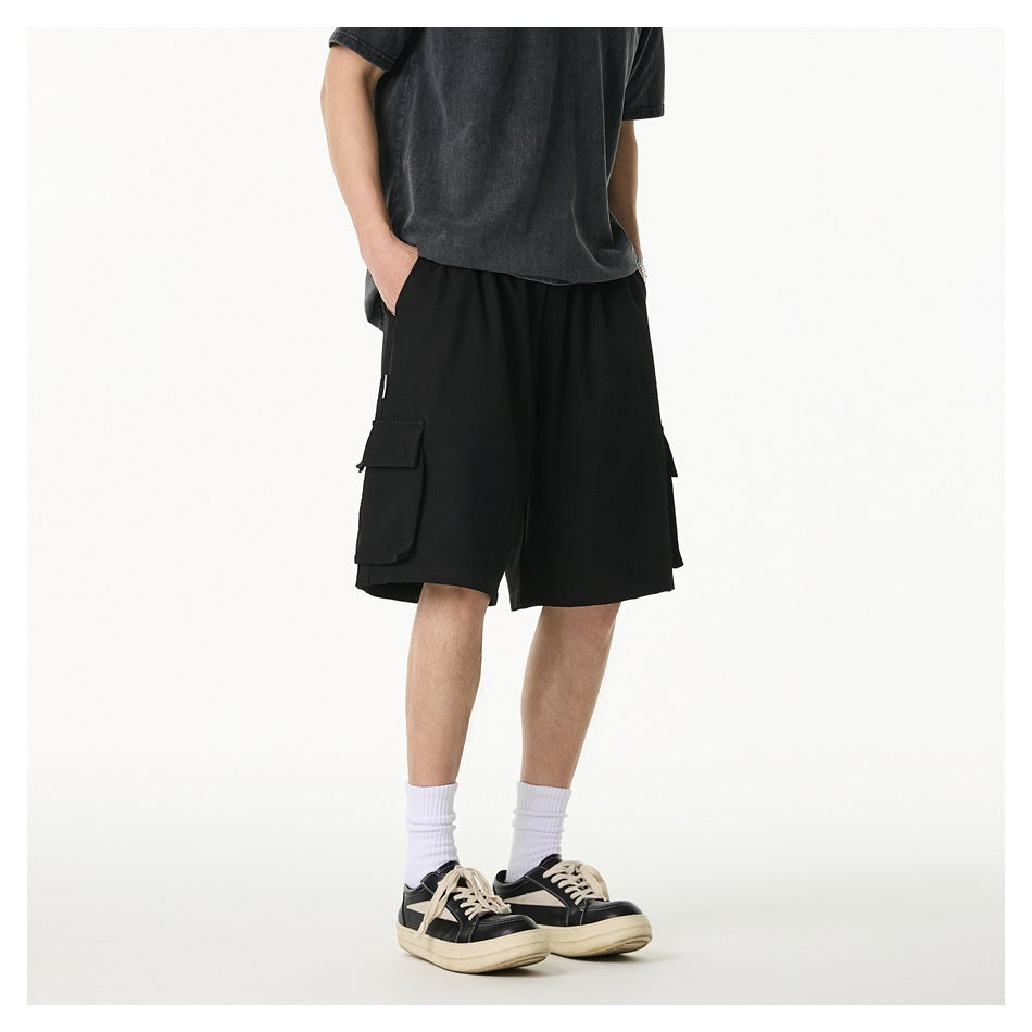 Front three-quarter view of a model wearing loose black cargo shorts with flap pockets and a dark T-shirt.