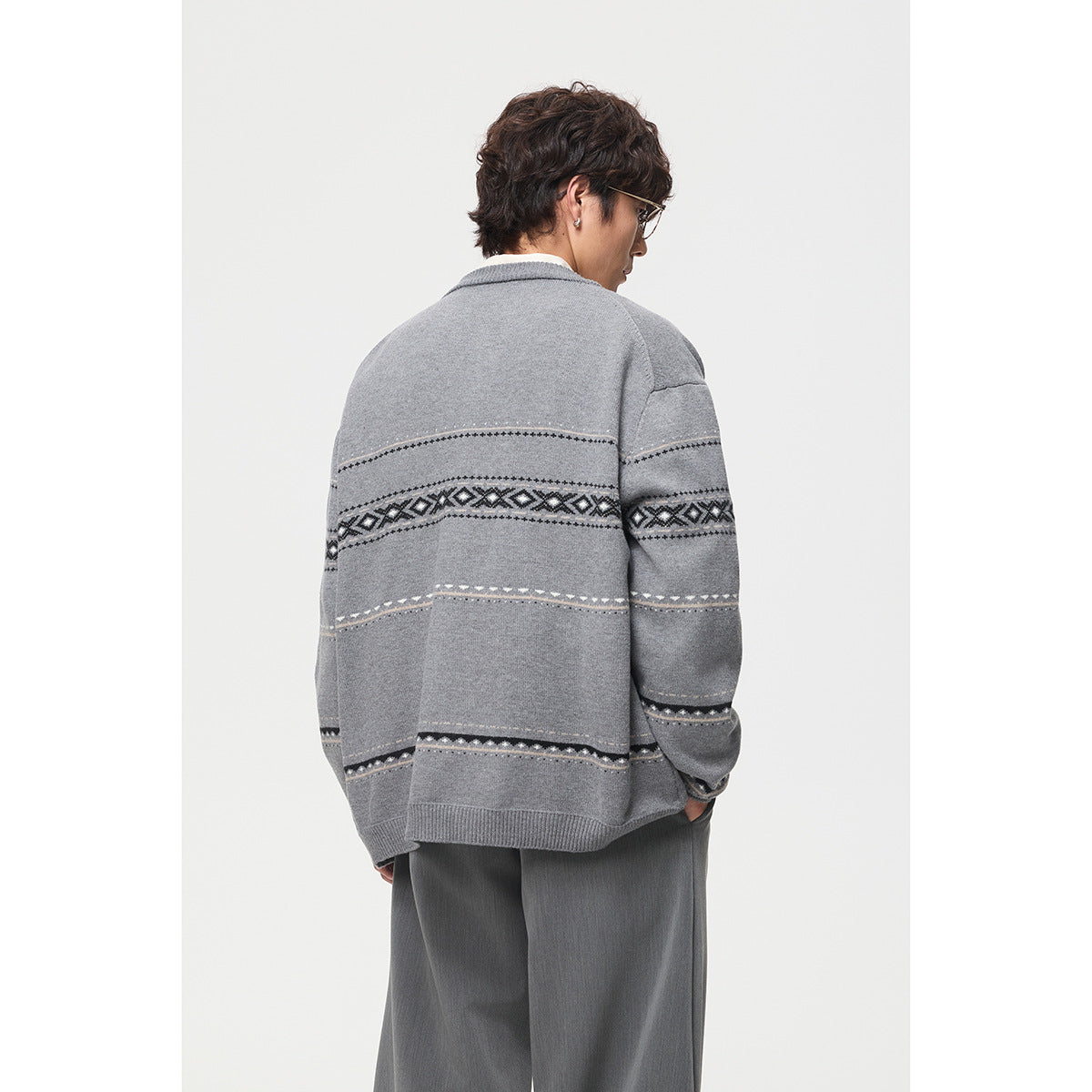 Back view of a man wearing a gray button-front cardigan with black and white geometric stripe patterns.