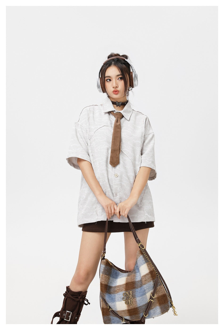 Model wearing an oversized pale gray patterned short-sleeve button-up shirt with a brown tie and dark brown skirt.