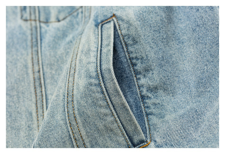 Close-up of a slanted pocket opening on a light blue denim jacket with double-stitched edges.