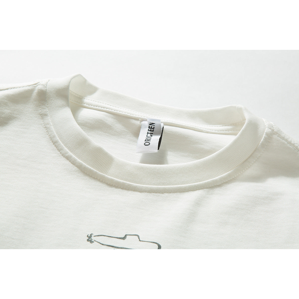 Close-up of an ivory T-shirt’s ribbed crew neck, sewn-in label, and partial small chest graphic.