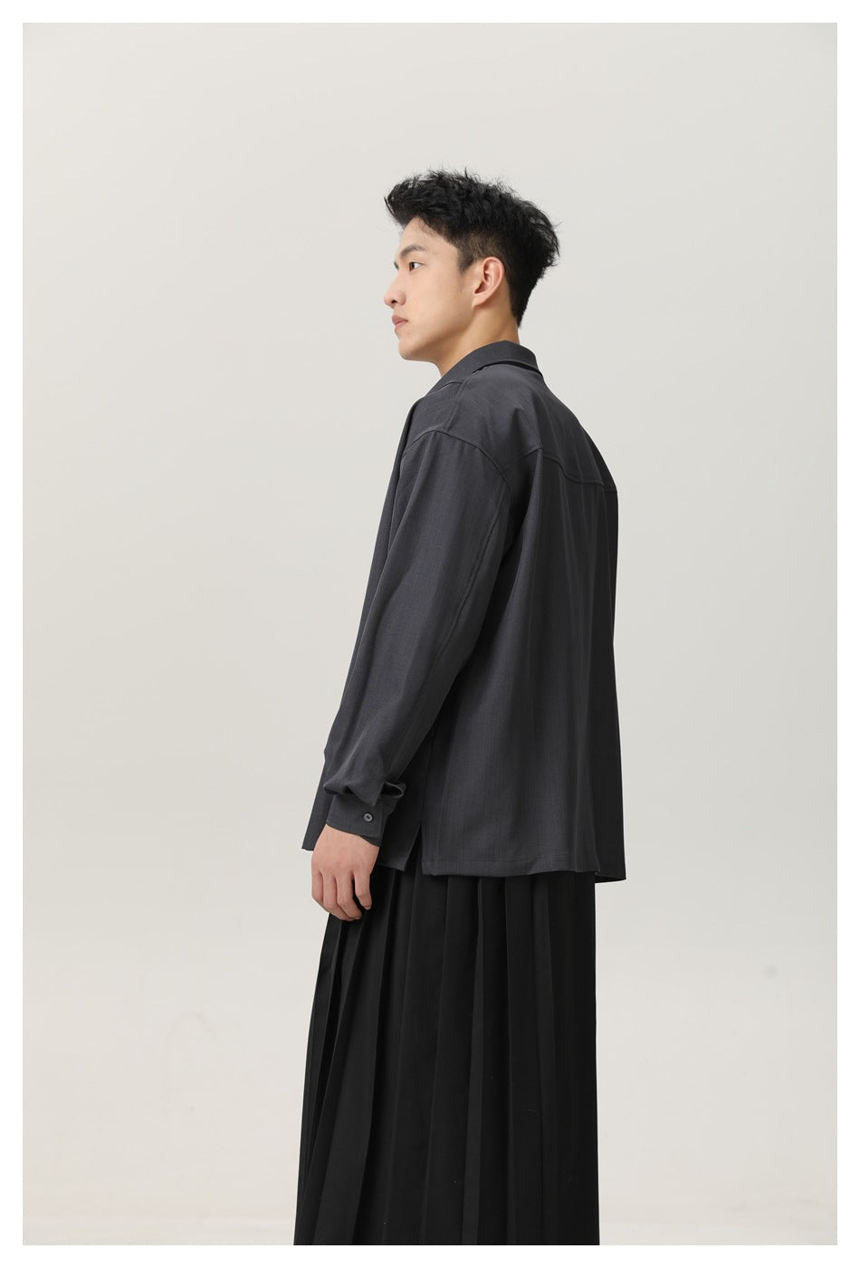 Side and rear view of a man wearing a charcoal long-sleeve shirt with a straight hem and black pleated skirt.