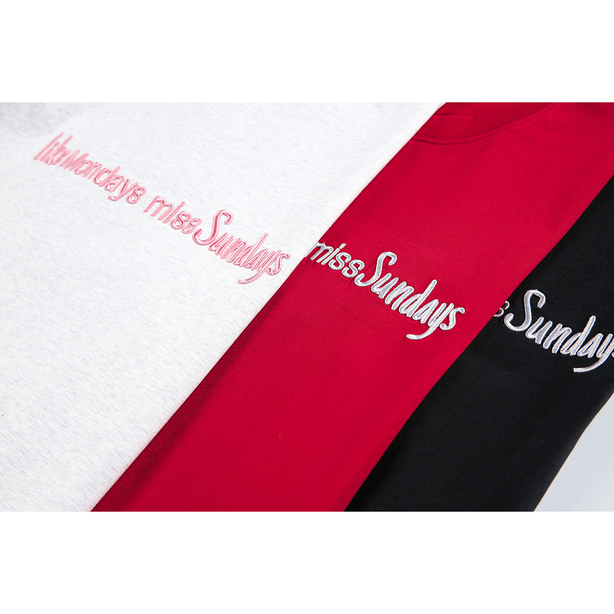 Close-up of embroidered “like Mondays miss Sundays” lettering on light gray, red, and black T-shirts.