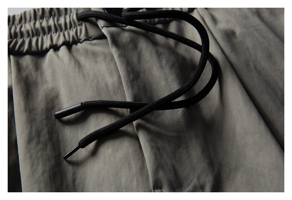 Close-up of gray shorts showing black drawcords and a stitched pocket opening.