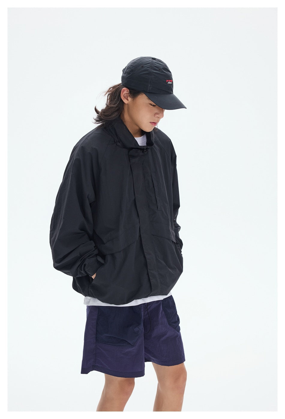Closer view of a model wearing a black oversized jacket and navy shorts with a black cap.