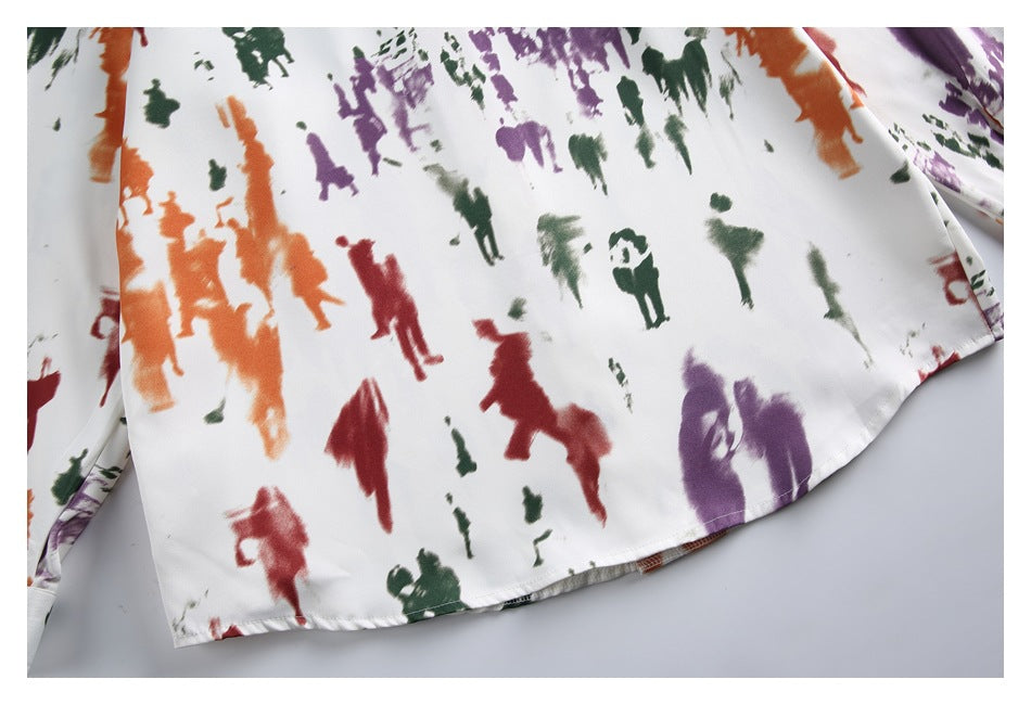 Close-up of the lower front of a cream shirt with multicolored abstract figures and a curved hem.