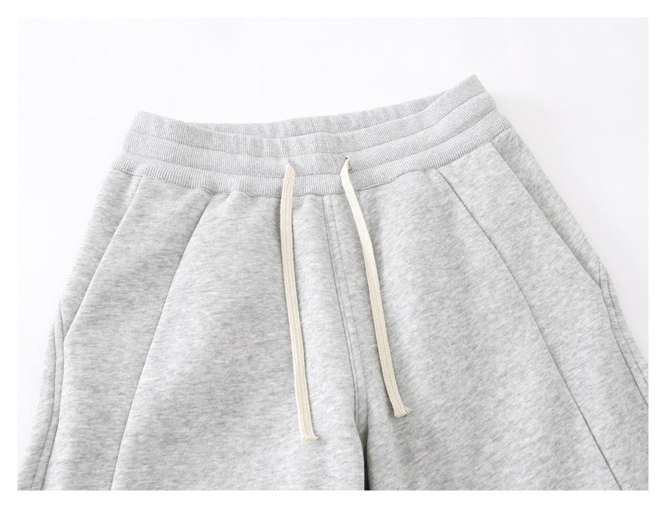 Close-up of light gray melange pants showing the elastic waistband, cream drawstrings, and front pocket seams.