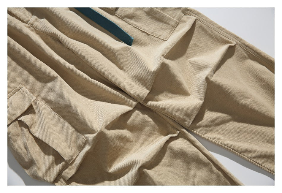 Close-up of tan ribbed trousers with stitched panels and a teal webbing belt.