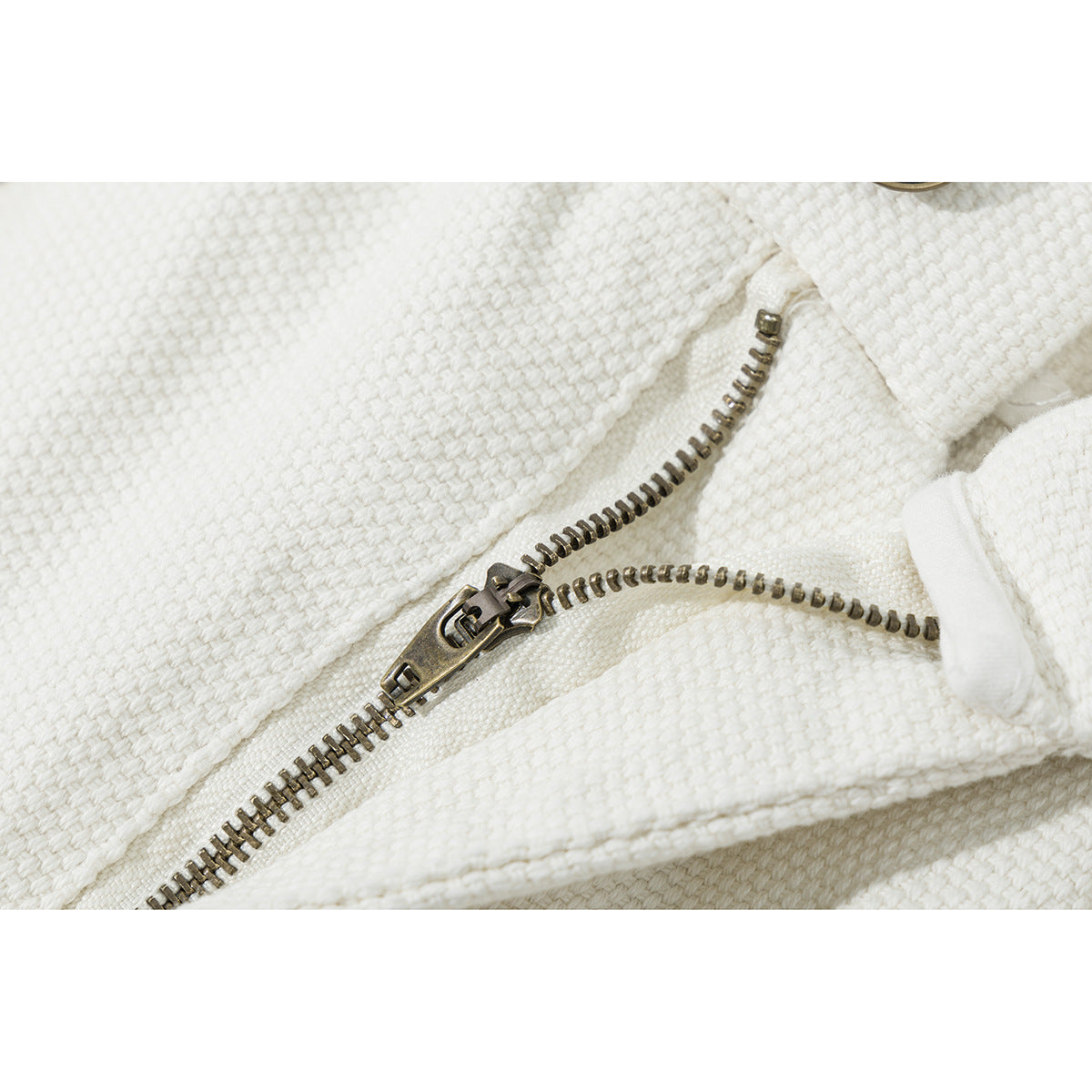 Close-up of an antique-brass zipper and ivory textured fabric on the shorts.