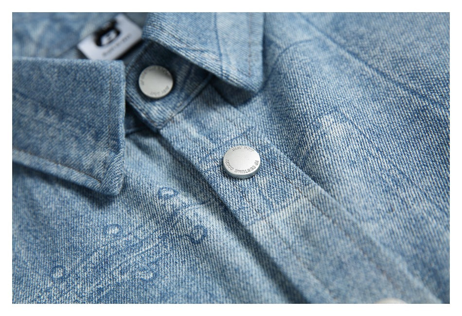 Detail of the shirt collar and placket with two silver snap buttons and a light blue patterned surface.
