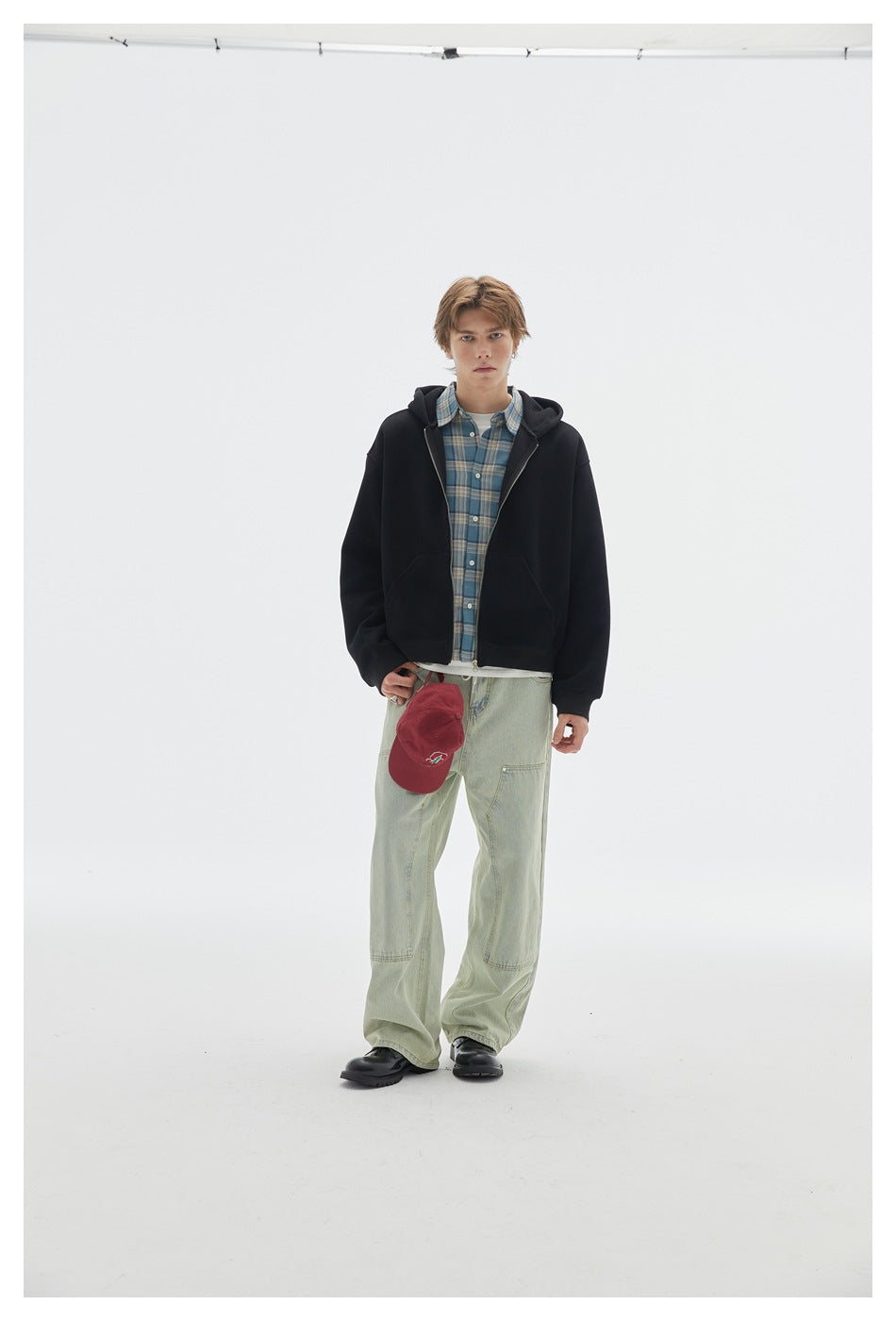 Front view of a model wearing a black zip-up hooded sweatshirt over a blue plaid shirt.