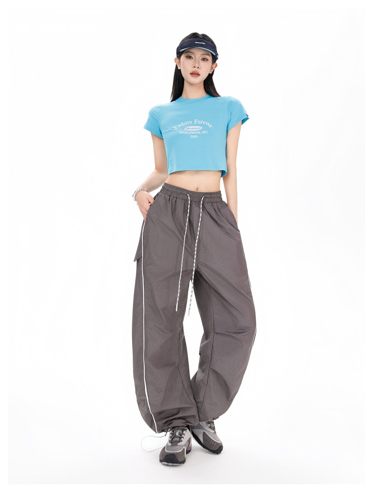 Full-length front view of a model wearing charcoal-gray wide-leg pants with white piping and a blue cropped T-shirt.