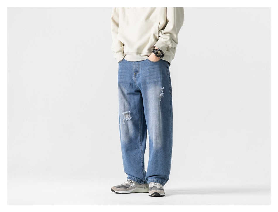 Full-length front view of a model wearing loose, distressed blue jeans and a cream sweatshirt.