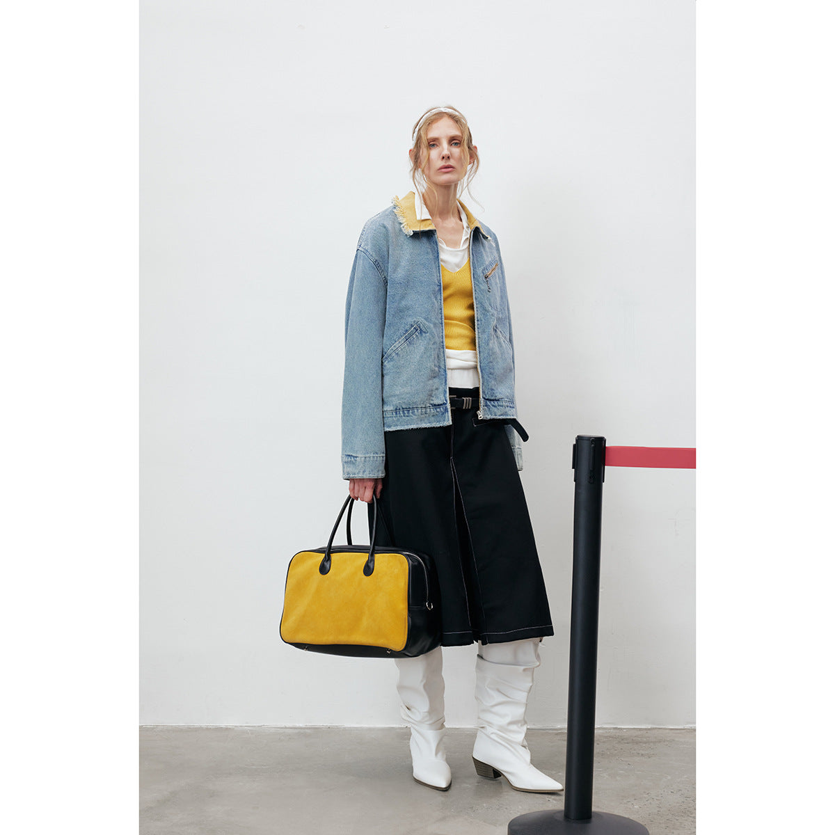 Model wearing a light blue denim jacket with a frayed yellow collar, styled with a yellow top, black skirt and white boots.