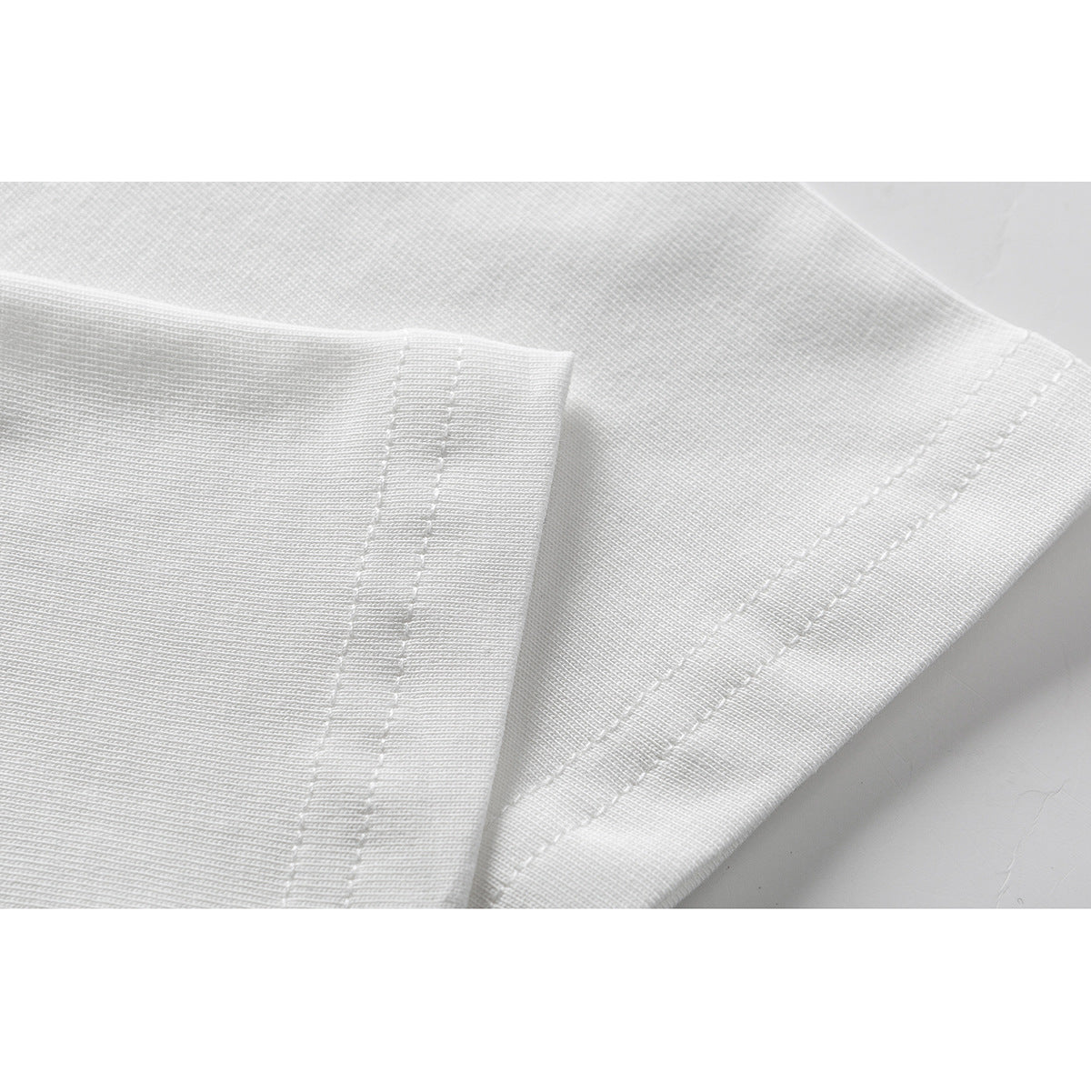 Close-up of a white T-shirt showing the sleeve and hem with parallel rows of stitching.