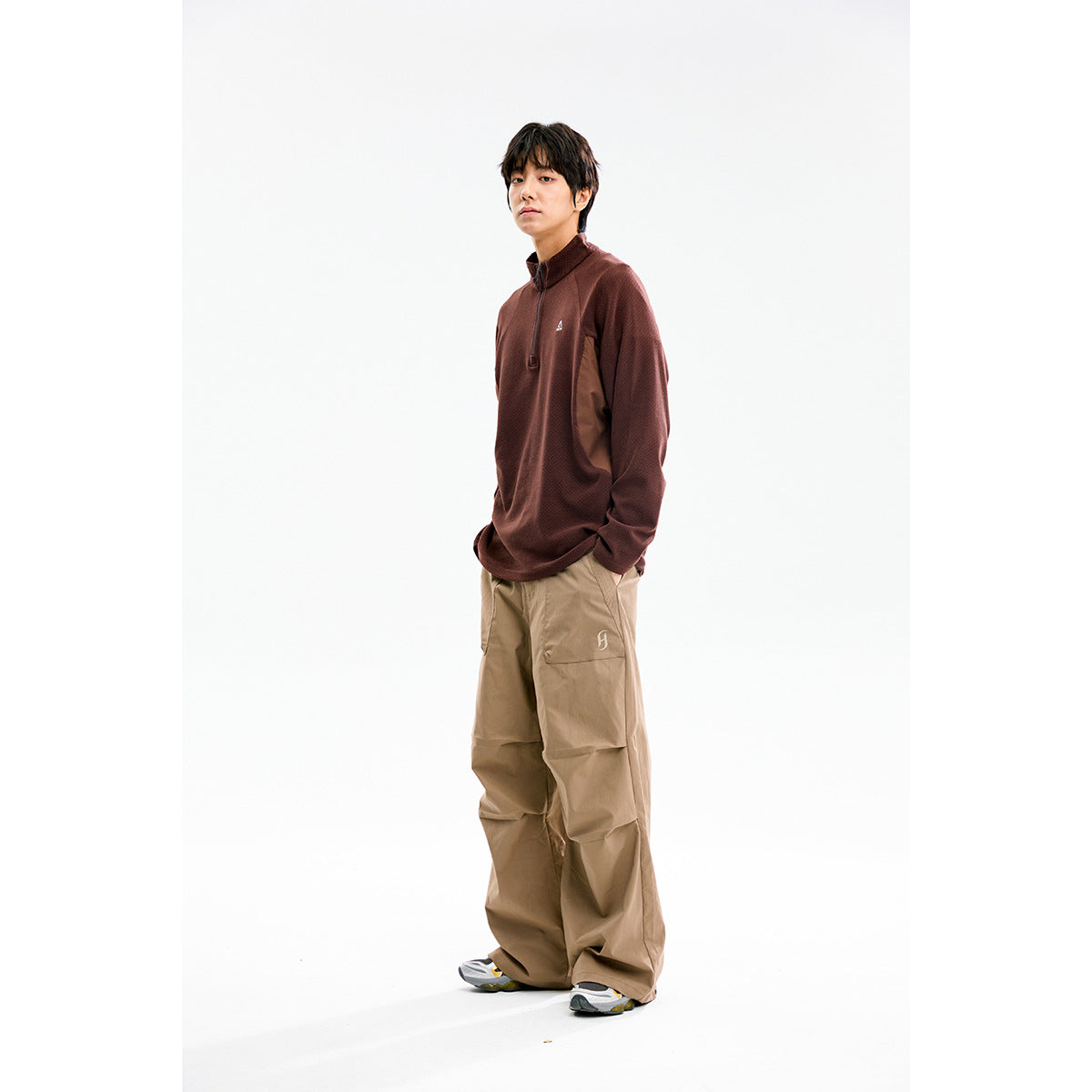 Model wearing a dark brown quarter-zip pullover with loose tan cargo pants against a white studio background.