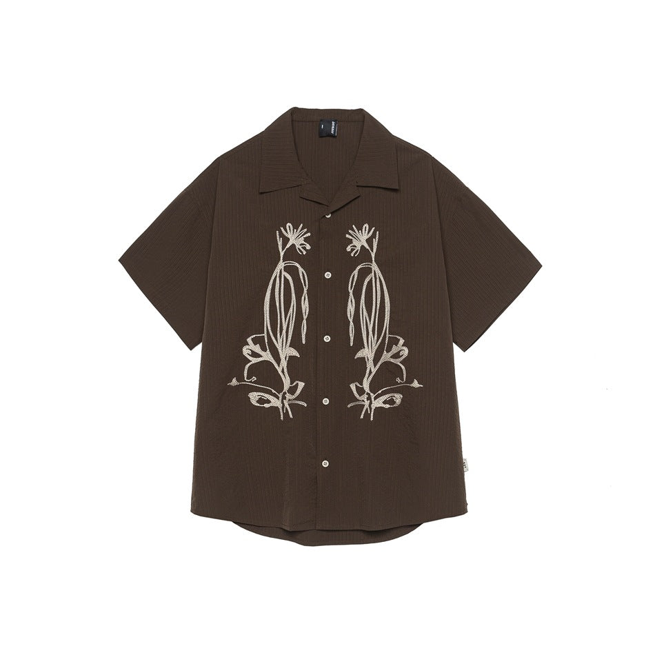 Brown short-sleeve camp-collar shirt with cream floral embroidery and buttons, front flat view on white