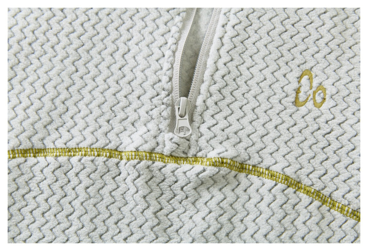 Close-up of a light gray zigzag-textured garment with a front zipper, yellow seam stitching and small yellow embroidery.