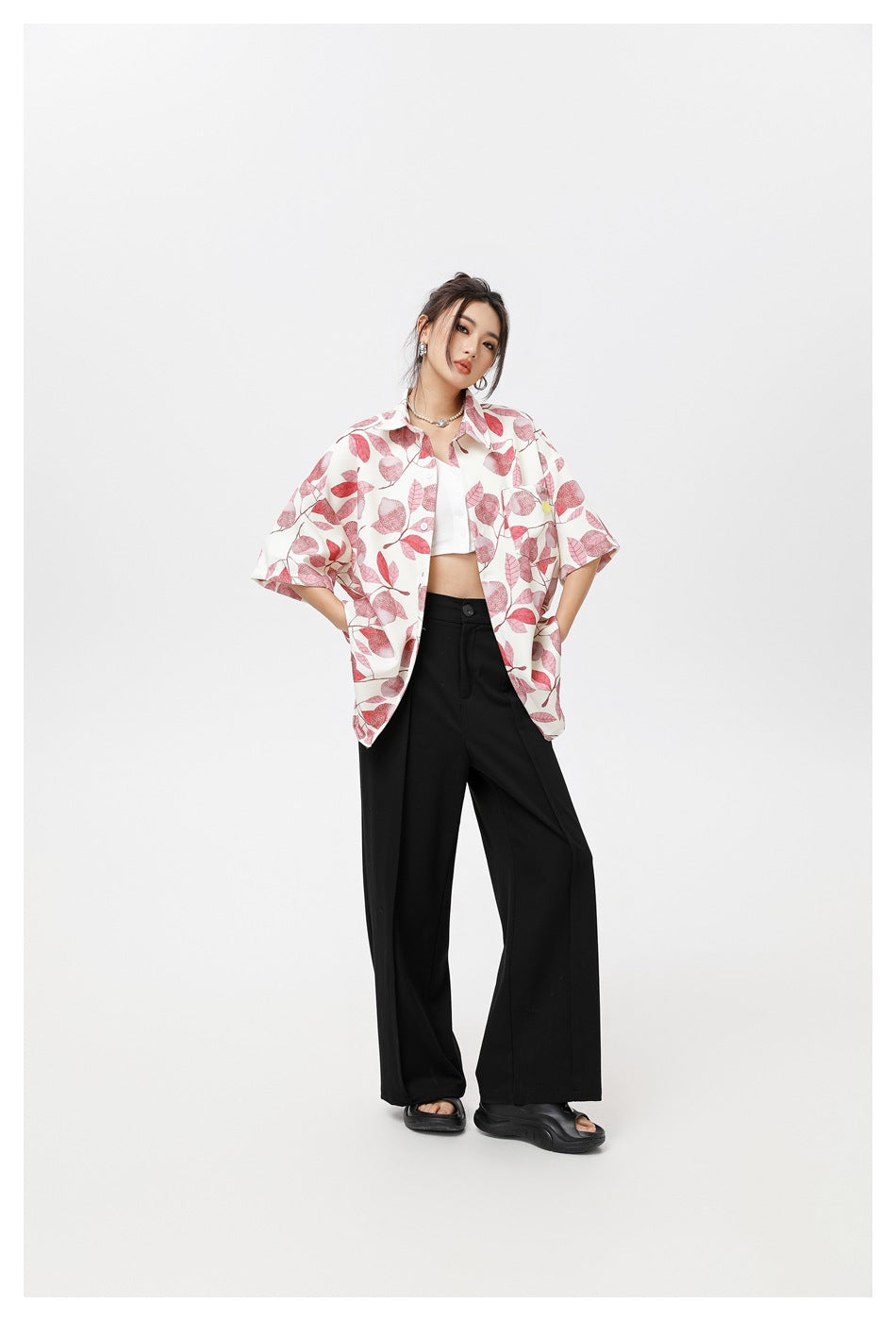 Model wearing an oversized ivory short-sleeve button-up shirt with a pink botanical print, styled with black trousers.