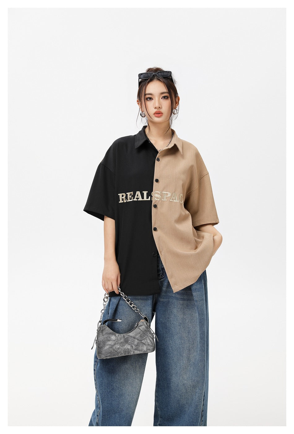 Model in oversized black and khaki split short-sleeve button shirt, loose blue jeans and a chain-strap gray bag