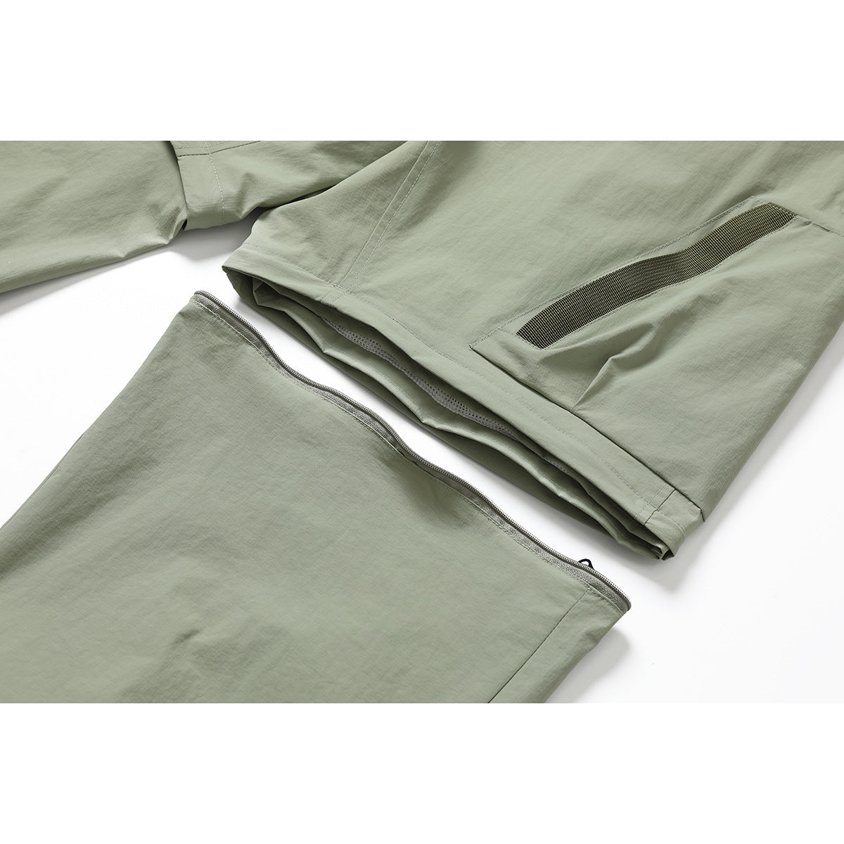 Close-up of pale sage-green pants showing a zippered section and a dark-trimmed leg pocket.