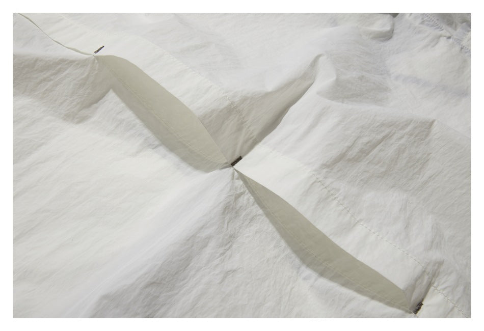Close-up of white garment panels with overlapping fabric tabs and small dark fasteners.
