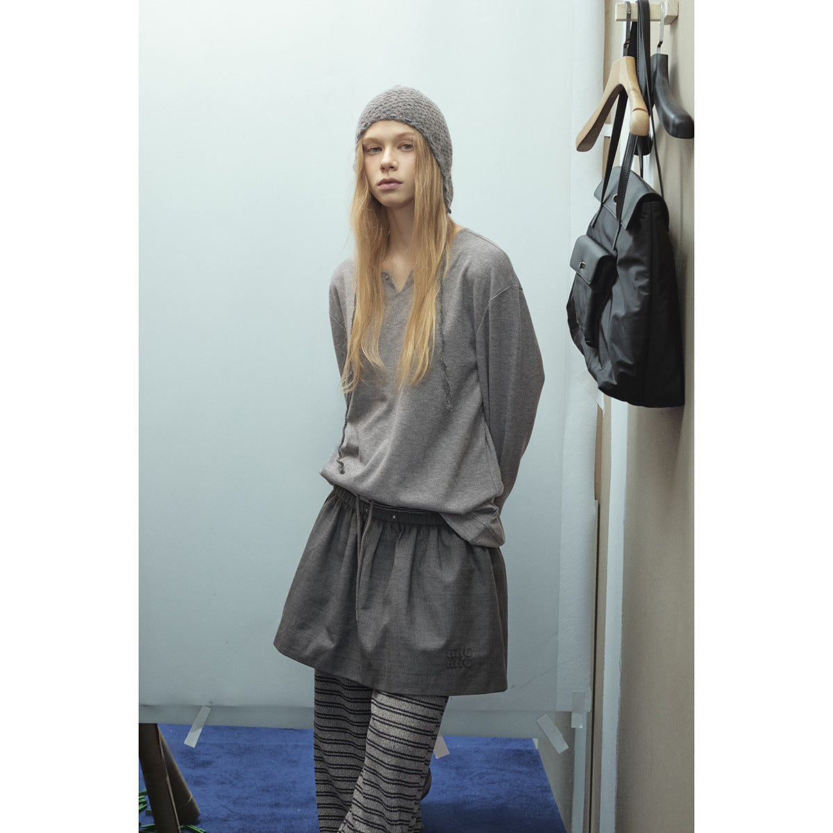 Model wearing a gray pullover and matching drawstring shorts over striped trousers, with a gray knit hat.