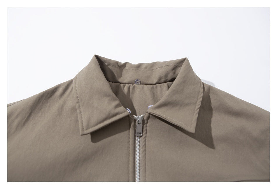 Close-up of the taupe jacket's pointed collar, buttoned inner neck tab, and silver front zipper.