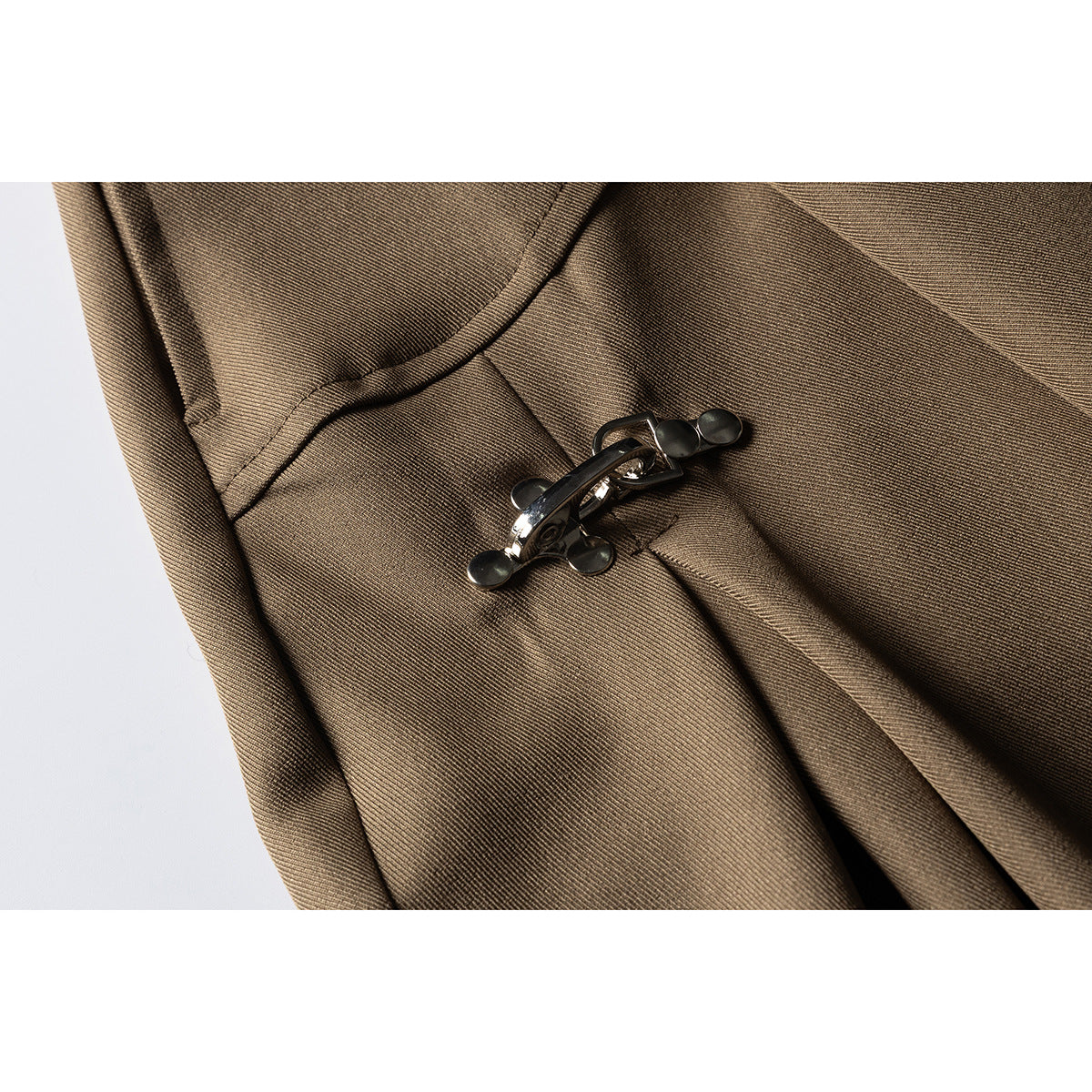 Close-up of a dark metal clasp fastening on brown shorts, with the fabric folds and stitching visible.