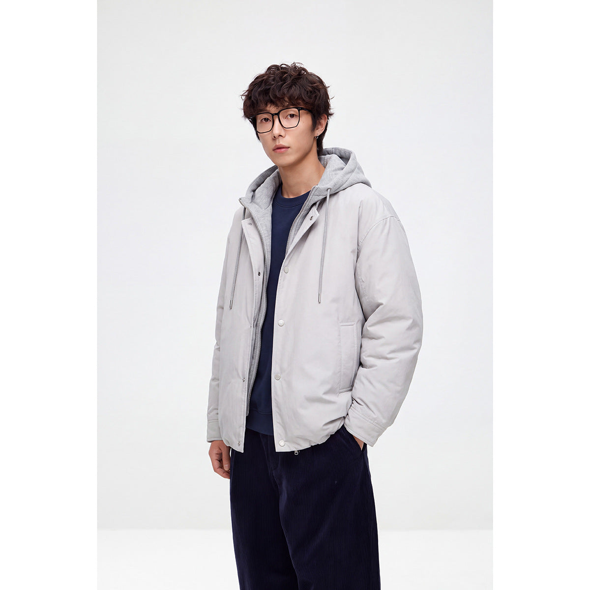 Three-quarter view of a model wearing a light gray hooded snap-front jacket with front pockets.