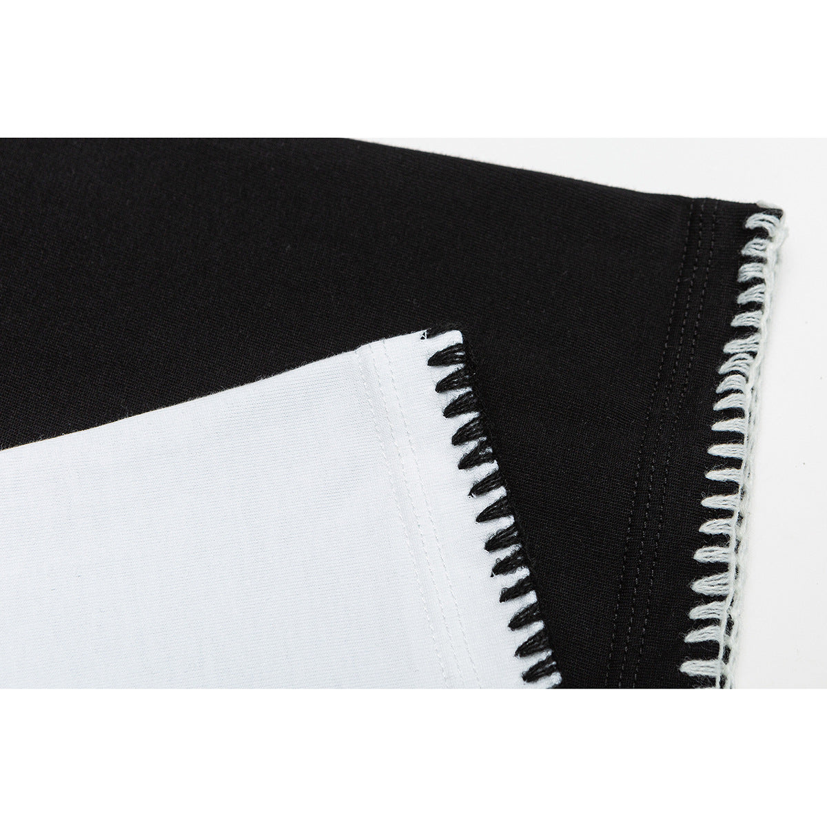 Close-up of black and white T-shirt fabric with contrasting blanket-stitched edges.
