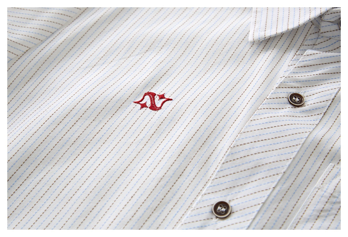 Close-up of a red embroidered emblem on a white shirt with fine blue and brown stripes.