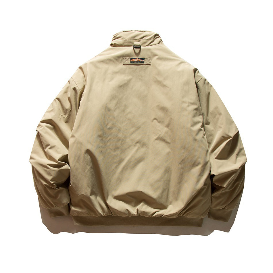 Back view of a light tan jacket with a stand collar, elastic cuffs and hem, and a small patch below the collar.
