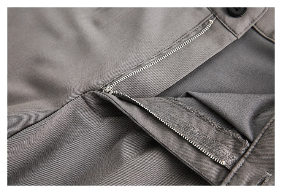 Close-up of gray trousers showing the metal zipper fly, waistband button, and stitching.