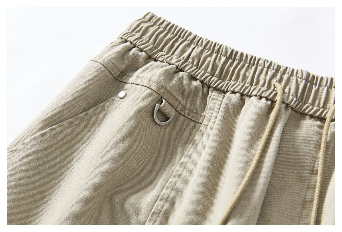 Close-up of the elastic waistband, drawstring, pocket seam, and metal loop on light khaki bottoms.