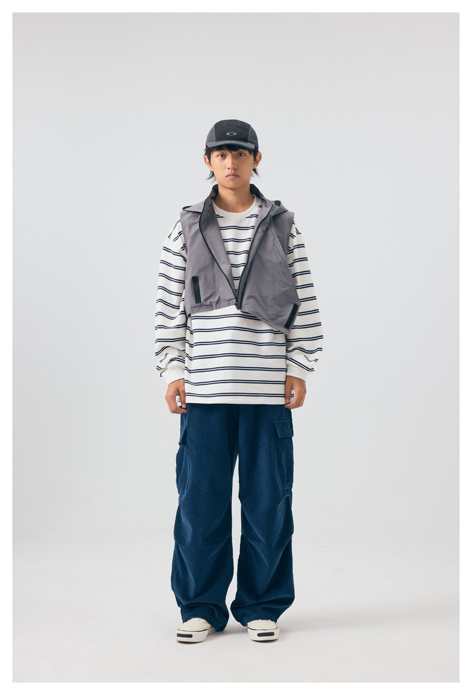Model wearing gray cropped hooded zip vest over a striped long-sleeve top and navy cargo pants, front view