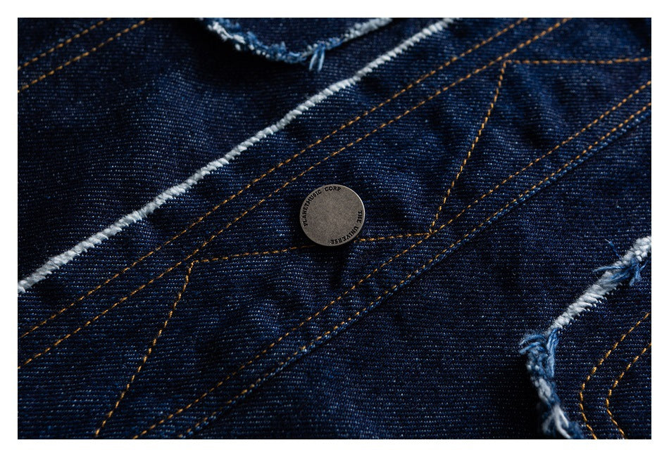 Close-up of a small round metal button on dark indigo denim with gold stitching and frayed seams.