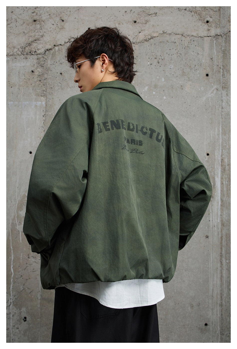 Back view of a model wearing a dark olive jacket with large English lettering printed across the upper back.