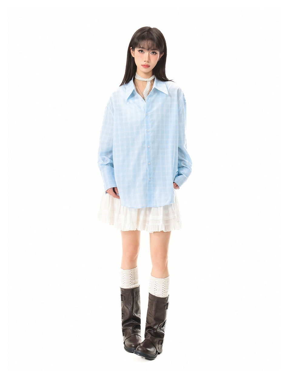 Full-length view of a model wearing a light-blue plaid button-up shirt over a white ruffled mini dress and tall boots.
