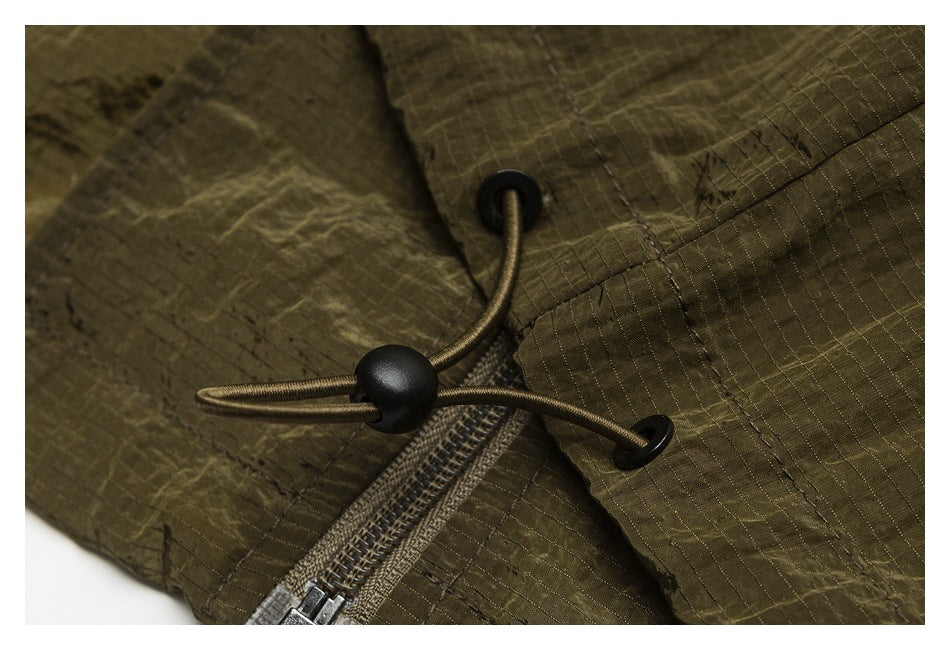 Close-up of olive fabric with a black cord toggle, drawcord, and zipper.