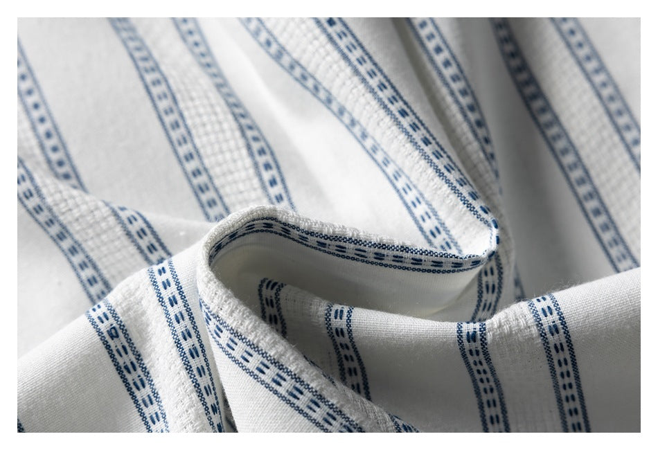 Close-up of a folded edge on white shirt fabric with narrow blue stripes and textured woven bands.